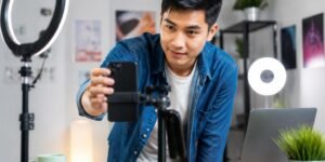 A young adult adjusting a smartphone on a tripod in a bright room, preparing to record a video.